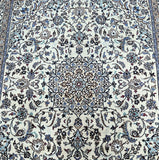 A close-up of a fine Persian Nain rug with a geometric medallion floral design in beige, blue, burgundy, and brown tones.