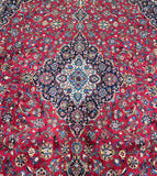 A detailed shot of an oversized Persian Kashan rug with a central medallion floral design, featuring a mix of red, blue, beige, green, yellow, brown, and orange tones on a cotton base.