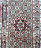 A hand-knotted Persian rug with a geometric herati design in beige, gold, red, black, light blue, pink, and orange tones.