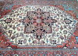 A hand-knotted Persian Heriz rug with a geometric design featuring beige, terracotta, black, pink, French blue, and gold tones.
