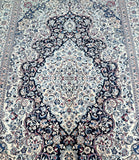 A detailed shot of a Persian Nain rug with a central medallion floral design, featuring silk-inlaid patterns in beige and indigo blue tones on a cotton base.