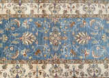 A hand-knotted wool rug with a floral pattern in light blue, beige, gray, maroon, and brown tones on a cotton base.