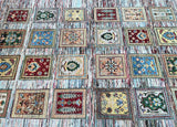A multicolored handmade Afghan Chobi rug with a floral and geometric pattern, featuring a mix of beige, brown, green, and other colors, placed on a striped background.