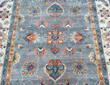 A decorative, handmade Afghan Chobi rug with a floral and geometric pattern in beige, gray, red, green, and blue.