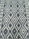 A rectangular, hand-woven kilim rug featuring a geometric tribal design in neutral beige and grey tones.