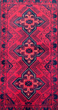 A close-up of a patterned Afghan rug featuring three large central medallions and a decorative border. The color palette is dominated by a bright red field, with dark navy blue and black geometric and floral motifs.