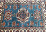 A multicolored, geometric-patterned Kazak rug with a central geometric design and a border featuring floral patterns in a variety of colors including blue, beige, maroon, orange, and green.
