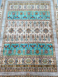 A rectangular hand knotted Afghan super Kazak rug with a geometric and floral pattern in beige, brown, turquoise, orange, and grey tones.