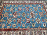 A traditional Afghan super Kazak area rug with a vibrant blue field, featuring intricate red, beige, and brown geometric medallions and floral motifs, finished with a detailed patterned border.