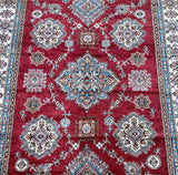 Close-up view of a handmade Afghan Super Kazak rug featuring a geometric design with red, blue, beige, green, and orange colors.
