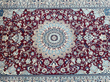 A fine Persian Nain rug with a central medallion floral design and arabesque motifs, in red, beige, burgundy, blue, and black colors.