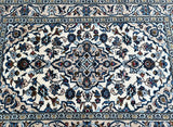A hand-knotted Persian Kashan rug with a central medallion floral design, featuring beige, blue, orange, red, and brown tones, on a cotton base.