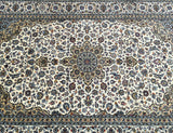 A signed Persian Kashan rug with a floral medallion design in beige, indigo blue, light blue, orange, and green tones on a cotton base.