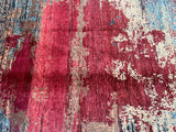 A close-up of a contemporary handmade Afghan Gabbeh rug with a central focus on the intricate pattern and colors, including red, beige, blue, and brown.