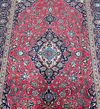 A traditional hand-knotted Persian Kashan rug with a central medallion floral design, in red, beige, black/indigo blue, and aqua blue tones.