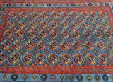 A vibrant handmade Afghan Roshnai rug with a geometric Bokhara design in blue, red, orange, black, and beige colors on a cotton base.