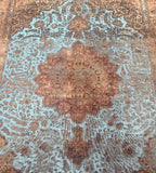 A vintage Persian Tabriz rug with a central medallion floral design, featuring a mix of light blue, gold, charcoal, and grey tones on a brown base.