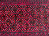 A close-up image of a tribal Persian Balouchi rug with a geometric pattern featuring black, red, beige, and orange tones.