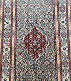 A close-up view of a hand-knotted Persian Birjand hall runner featuring intricate geometric patterns and a central medallion design in beige, blue, yellow, maroon, and green tones.
