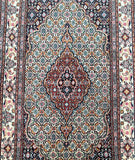 A close-up of a intricately designed Persian rug with a geometric pattern and a central medallion in a beige background.