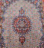 A detailed view of a traditional Persian Mood area rug with an intricate floral and geometric pattern in blue, rust red, beige, and brown.