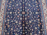 A traditional Persian Birjand rug featuring an all-over floral design with indigo blue, beige, green, orange, and light blue tones.