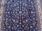 A traditional Persian Birjand area rug with a deep navy blue field, featuring an intricate floral and vine pattern in cream, red, orange, and light blue, finished with a detailed multi-colored border.