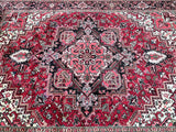 A traditional Persian Heriz area rug with an intricate floral and geometric pattern, featuring a dominant red field with black, pink, and beige details.