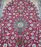 A close-up of a fine Persian Isfahan rug featuring a central medallion floral design in red, beige, gold, and blue tones.
