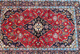 A traditional Persian Kashan rug with a central medallion floral pattern, featuring a geometric design in a multitude of colors including red, beige, blue, and yellow.