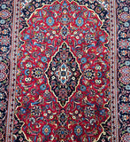 Close-up of a Persian Kashan rug showcasing a central medallion floral pattern with a rich color palette including red, beige, blue, and green tones.