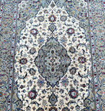 A hand-knotted beige Persian Kashan rug with a central medallion floral design, featuring a dense pure lamb's wool pile on a cotton base, and dyed in beige, blue, pistachio, olive, red, and orange tones.
