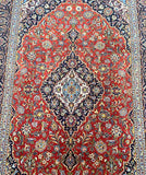 A detailed image of a fine Persian Kashan rug with a central medallion floral design, featuring a combination of orange, red, blue, beige, yellow, green, and pink tones.