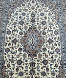 Close-up view of a beige Persian Kashan rug featuring a central medallion floral design with intricate patterns in blue, brown, and red tones.
