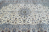 A traditional Persian Kashan area rug with an intricate floral and vine pattern, featuring a cream background with blue, gray, and gold accents.