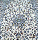 A traditional Persian Kashan area rug with an intricate floral and medallion pattern, featuring a cream background with blue, gray, and gold accents.
