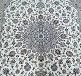 A close-up of an ornate Persian Kashan area rug featuring a central medallion and intricate floral motifs in cream, gray, blue, and brown tones.