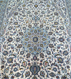 A beige tone Persian Kashan rug with a central medallion floral design and paisley motifs, featuring touches of blue, pistachio green, and brown.