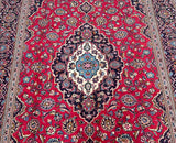 A traditional Persian Kashan rug featuring a central medallion floral design with red, beige, light blue, mustard, and indigo blue color tones.