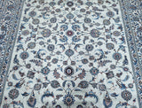 A hand-knotted Persian Kashan rug with a floral design in beige, blue, and gray tones, featuring a cotton base and traditional knotting techniques.