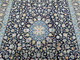 A traditional Persian Kashan area rug with an intricate floral and medallion pattern, featuring a dark navy blue field with cream, beige, light blue, and orange accents