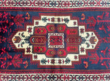 A hand-knotted tribal Persian Luri rug with a geometric medallion design in deep colors on a light background, featuring a central medallion and bordered with a pattern of diamonds and triangles.