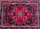 A hand-knotted Persian village Malayer rug with a central medallion featuring broken branches in a semi floral, semi geometric pattern, in a color palette of red, indigo blue/black, pink, orange, brown, and light blue.
