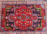 A hand-knotted Persian village Malayer rug with a geometric pattern featuring a central medallion with broken branches, in a color palette of red, indigo blue/black, pink, orange, green, brown, and light blue.