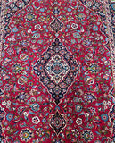 A traditional Persian Mashad rug with a dense pile, featuring a central medallion floral royal design and a border in a red, blue, orange, beige, pink, and green tone dyed using traditional methods.