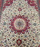 Close-up of a Persian Mashad rug featuring a central medallion floral design with red, blue, and beige colors on a beige background.