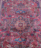 A close-up of a traditional Persian Mashad rug with a complex geometric and floral pattern in shades of red, blue, beige, and brown.