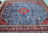 A large traditional oriental Meymeh rug with a complex geometric pattern, featuring a dominant blue field, a red central medallion, and a dark brown border with intricate white and red details.