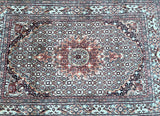 A hand-knotted Persian rug with a central medallion fish design, featuring a multicolored pattern with beige, terracotta red, pink, black, and aqua blue tones.