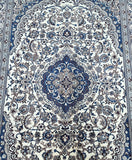 Close-up of a Persian Nain rug featuring a central medallion floral design with beige, blue, brown, and burgundy tones on a light background.